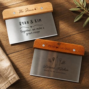 May include: Two stainless steel dough scrapers with wooden handles. The top scraper features the text The Shaws, RYAN & KIM, and Together, we make a great recipe. The bottom scraper features TEDD & LARANA, Larana Kitchen, and MADE TO BE SAVOURED.