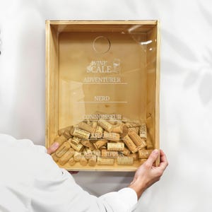 May include: A wooden box with a glass front filled with wine corks. The box has a label that reads "Wine Scale" and includes categories for wine drinkers: "Adventurer", "Nerd", "Connoisseur", "Explorer", and "Casual Sipper".