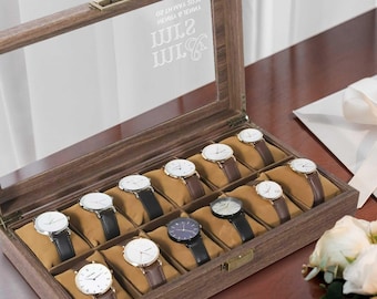 May include: A wooden watch box with a glass lid and 12 compartments for storing watches. The box has a personalised inscription on the top that reads "WM & WM 2022 NEWLY WEDS".