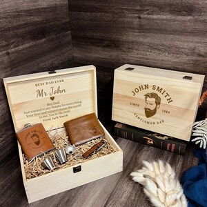 May include: A wooden gift box with a personalized message for "Mr John" and a smaller wooden box with the text "John Smith Since 1984 Gentleman Dad". The gift box contains a brown leather wallet, a flask, two shot glasses, and a bottle opener.