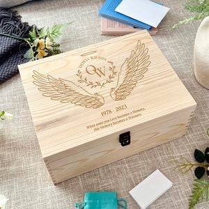 May include: A wooden keepsake box with an engraved design of angel wings and a monogram with the name Olivia Wilson and the dates 1978-2023. The inscription reads "When some you Love becomes a Memory, this Memory becomes a Treasure."