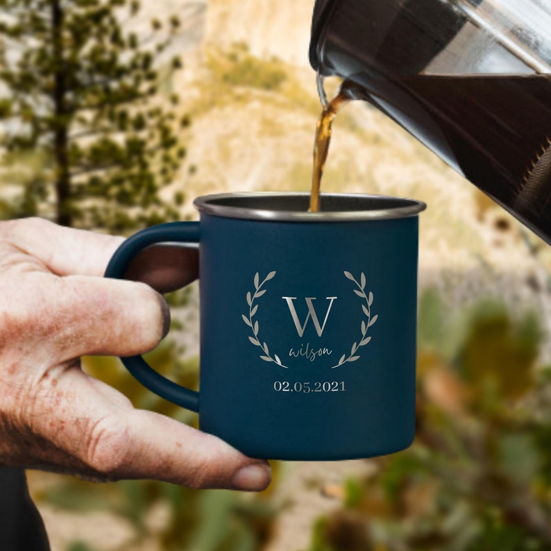 May include: A dark blue enamel camping mug with a white wreath and the letter "W" and the text "wilson 02.05.2021".