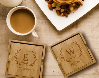 Puede incluir: Dos posavasos cuadrados de madera con iniciales y nombres grabados. El primer posavasos tiene la letra "E" y el nombre "emily" con la fecha "EST. 1999". El segundo posavasos tiene la letra "W" y el nombre "wilson" con la fecha "EST. 1991".