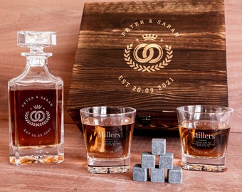 Può includere: Una scatola di legno con un design inciso personalizzato che presenta i nomi "Peter & Sarah" e la data "EST 20.09.2021". La scatola contiene due bicchieri di whisky in vetro trasparente con i nomi "Millers" e la data "August 08, 2020" incisi su di essi. È incluso anche un decanter in vetro trasparente con un tappo. La scatola è accompagnata da un set di cubetti di raffreddamento per whisky in pietra grigia.