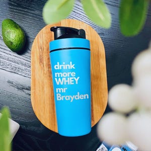 May include: A blue shaker bottle with a black lid and a white inscription that reads "drink more WHEY mr Brayden".
