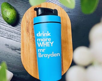 May include: A blue shaker bottle with a black lid and a white inscription that reads "drink more WHEY mr Brayden".