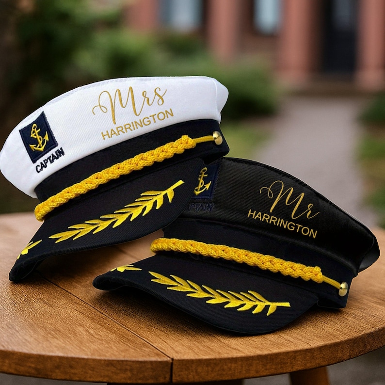 May include: Two captain's hats, one white and one black, with gold accents. The white hat has "Mrs Harrington" and "Captain" text, while the black hat says "Mr Harrington". Both hats feature an anchor emblem and gold rope trim.