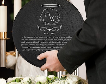 May include: A black slate plaque with a white engraved design. The design includes a halo, wings, a heart, and the initials "O.W." with the text "1978 2023" below. The plaque also includes the text "In the tapestry of our memories, you're woven in as our guiding. Your love and light continue to grace our lives, gently guiding us each moment. Though you've ascended to a higher realm, presence remains, watching over us with a love that transcends bounds. Forever in our hearts, you are our cherished guiding us through life's journey with whispers."