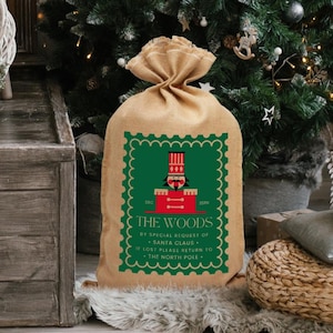 Puede incluir: Un saco de arpillera marrón con un diseño verde y rojo. El diseño presenta un cascanueces y el texto "THE WOODS BY SPECIAL REQUEST OF SANTA CLAUS. IF LOST PLEASE RETURN TO THE NORTH POLE."