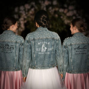 Könnte beinhalten: Drei Jeansjacken mit Perlenbesatz und individuellem Text. Eine Jacke trägt die Aufschrift "Nicole Bride to Be" mit Datum und Jahr. Eine andere sagt "Nicole's Bride Club". Die dritte Jacke trägt die Aufschrift "Ametia Maid of Honour".