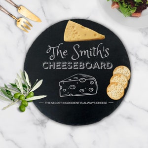 以下が含まれることがあります： 黒いスレート製のチーズボードに、「The Smith's Cheeseboard」と「The secret ingredient is always cheese」という白い文字が書かれています。ボードには、くさび形のチーズとブロックチーズのイラストが描かれています。