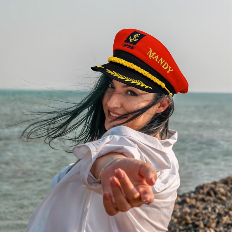 May include: A red and black captain's hat with gold trim and the name "Mandy" embroidered on the side. The hat features a gold anchor emblem and the word "CAPTAIN".