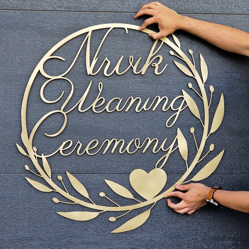May include: Gold metal wreath with the words "Nuvk Wedding Ceremony" and a heart shape in the center.