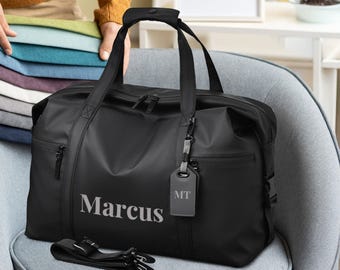 May include: Black travel duffel bag with a zipper closure and a personalized name tag that says "Marcus" and "MT".