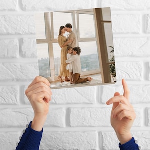 Könnte beinhalten: Eine vierköpfige Familie posiert für ein Foto in einem hellen Raum mit großen Fenstern. Die Eltern stehen eng beieinander, während die beiden Kinder vor ihnen stehen. Die Eltern schauen sich an, während die Kinder in die Kamera schauen. Die Familie ist leger gekleidet. Das Foto wurde aus einem leicht erhöhten Winkel aufgenommen.