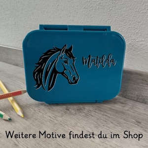 Könnte beinhalten: Eine türkisfarbene Brotdose mit einer schwarzen Pferdekopf-Silhouette und dem Namen "Matilda" in Schreibschrift. Die Brotdose ist rechteckig mit einem Klappdeckel. Der Text "Weitere Motive findest du im Shop" steht unten.