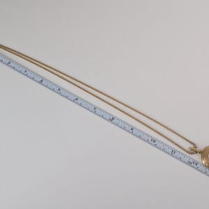 May include: Gold-toned pendant necklace with a round, ornate pendant. The pendant features a white center with a design. The chain is long and delicate. The necklace is approximately 14 inches long.
