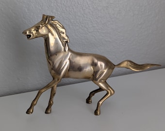 May include: A brass horse figurine in a dynamic pose, with its mouth open and tail flowing. The sculpture is detailed, showcasing the horse's muscles and mane. The figurine is a decorative item, likely for display.