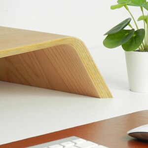 May include: A light wood laptop stand with a curved front edge. The stand is made of plywood and has a natural wood finish.