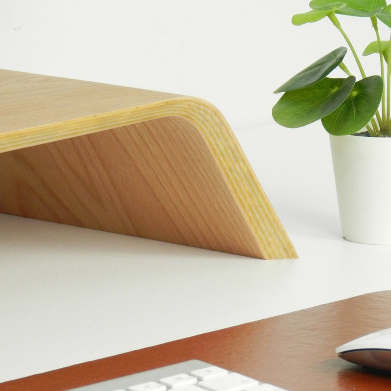 May include: A light wood laptop stand with a curved front edge. The stand is made of plywood and has a natural wood finish.