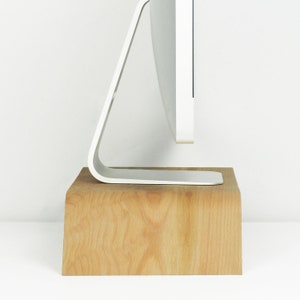 May include: A white computer monitor with a curved stand sits on a wooden riser. The riser is made of light brown wood with a natural grain pattern.