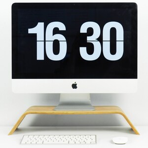 May include: A silver desktop computer with a black screen displaying the time 16:30. The computer is sitting on a wooden stand.