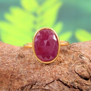 May include: A gold ring with a large, oval-shaped, faceted ruby gemstone.