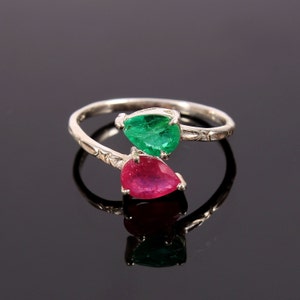 May include: A silver ring with a green emerald and a red ruby gemstone. The ring is designed with a twisted band and the gemstones are set in a pear shape.