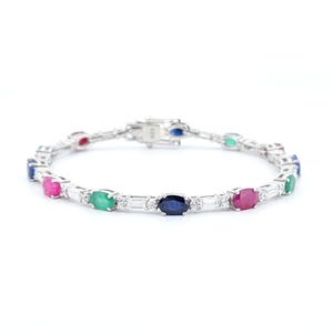 Puede incluir: Una pulsera de plata con una serie de piedras preciosas ovaladas en varios colores, incluyendo rojo, azul y verde. La pulsera también tiene piedras rectangulares y transparentes y un cierre.