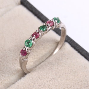 May include: A silver band ring with alternating green and red gemstones. The ring is set in a white metal band.