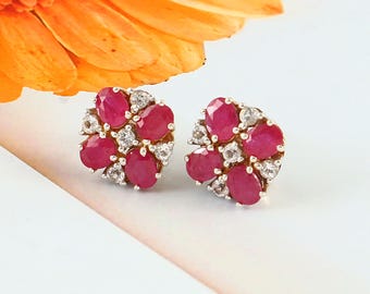 May include: A pair of silver stud earrings with a floral design. The earrings feature red and white gemstones.