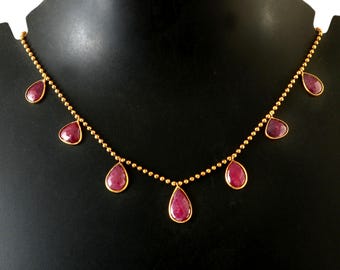 May include: A gold chain necklace with seven dangling teardrop-shaped ruby red stones.