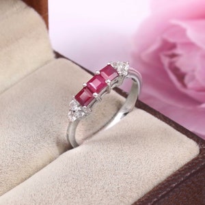 May include: A silver ring featuring three square red ruby stones and small white diamonds set in the band.