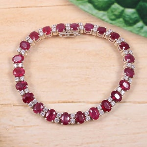 May include: A silver tennis bracelet featuring oval-shaped red rubies and smaller white diamonds set in the metal.