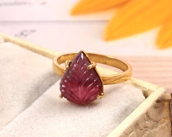May include: A gold ring with a carved pink gemstone in the shape of a leaf. The ring is in a white box.