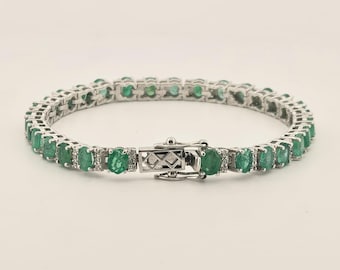 May include: A silver-toned tennis bracelet featuring a continuous row of oval-cut green emerald gemstones. Each emerald is separated by small, clear, round-cut accent stones set in a metallic frame, secured with a rectangular box clasp closure.