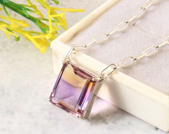 Può includere: Una collana con catena d'argento con un grande ciondolo rettangolare in ametista sfaccettata. Il ciondolo presenta un gradiente di tonalità viola e gialle.