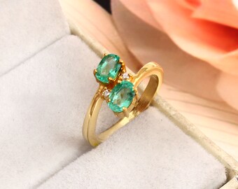 May include: A gold ring with two oval-shaped emerald gemstones and two smaller round diamonds. The ring is set in a delicate, twisted band.