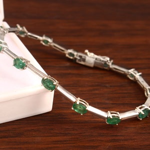 May include: A silver bracelet featuring a row of oval-shaped green emeralds. The bracelet has a clasp fastening.