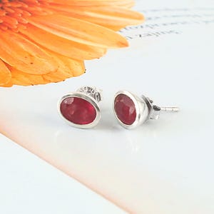 May include: A pair of silver stud earrings with oval-shaped red ruby gemstones.