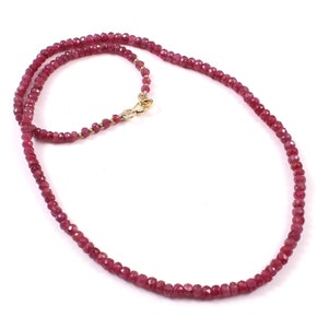 May include: A necklace composed of small, faceted, ruby-colored beads. The beads are strung together, forming a continuous loop. The clasp is gold-colored, and the necklace is displayed against a white background.