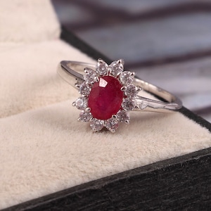 May include: A silver ring with a large oval ruby gemstone surrounded by smaller white gemstones.