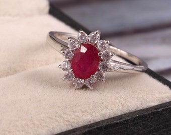 May include: A silver ring with a large oval ruby gemstone surrounded by smaller white gemstones.