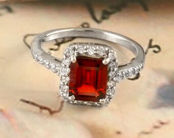 May include: A silver ring with a red gemstone surrounded by a halo of smaller white gemstones.