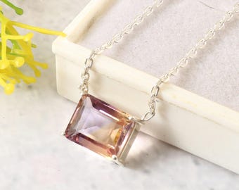 Può includere: Una collana con catena d'argento con un grande ciondolo rettangolare in ametista sfaccettata. Il ciondolo è un mix di tonalità viola, rosa e arancioni.