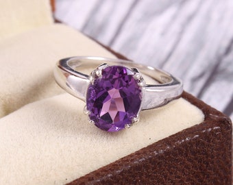 May include: A silver ring with a large, oval-shaped amethyst gemstone. The ring is set in a simple, elegant style.