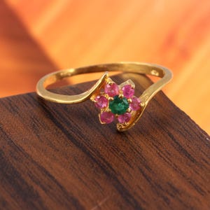 May include: A gold ring with a flower design featuring pink and green gemstones.