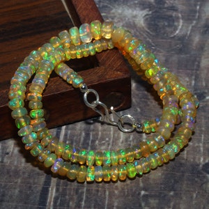 May include: A necklace made of small, rounded, iridescent opal beads. The beads show a range of colours, including yellow, green, and flashes of other hues. The necklace is fastened with a silver clasp.