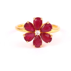 May include: A gold ring featuring a red ruby flower design. The centre of the flower has a small, clear diamond.