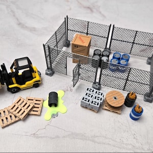 May include: Miniature industrial scene with a yellow forklift, wooden pallets, a chain-link fence, barrels, and a wooden crate. The scene includes a spill of green liquid and various other industrial elements.